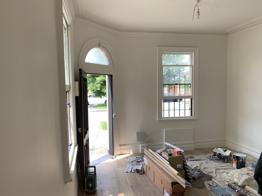 Freshly painted interior of a Fitzroy terrace — arched entry, ornate cornice, sash windows and drop sheets on the floor mid-job