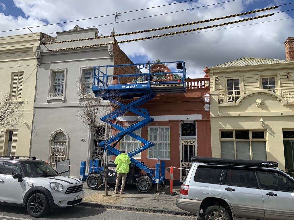 Scissor lift at the front of a heritage Fitzroy terrace row — elevated access required for ornate upper-storey facade work on a Victorian streetscape
