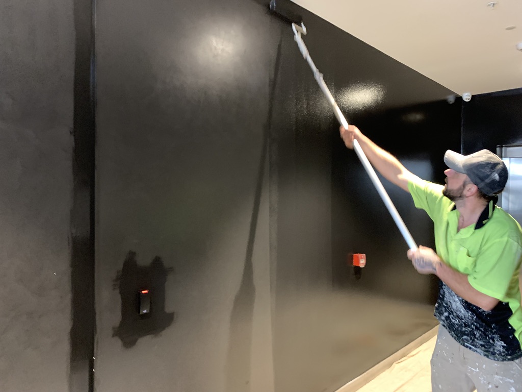 Painter rolling dark feature wall in Carlton apartment interior