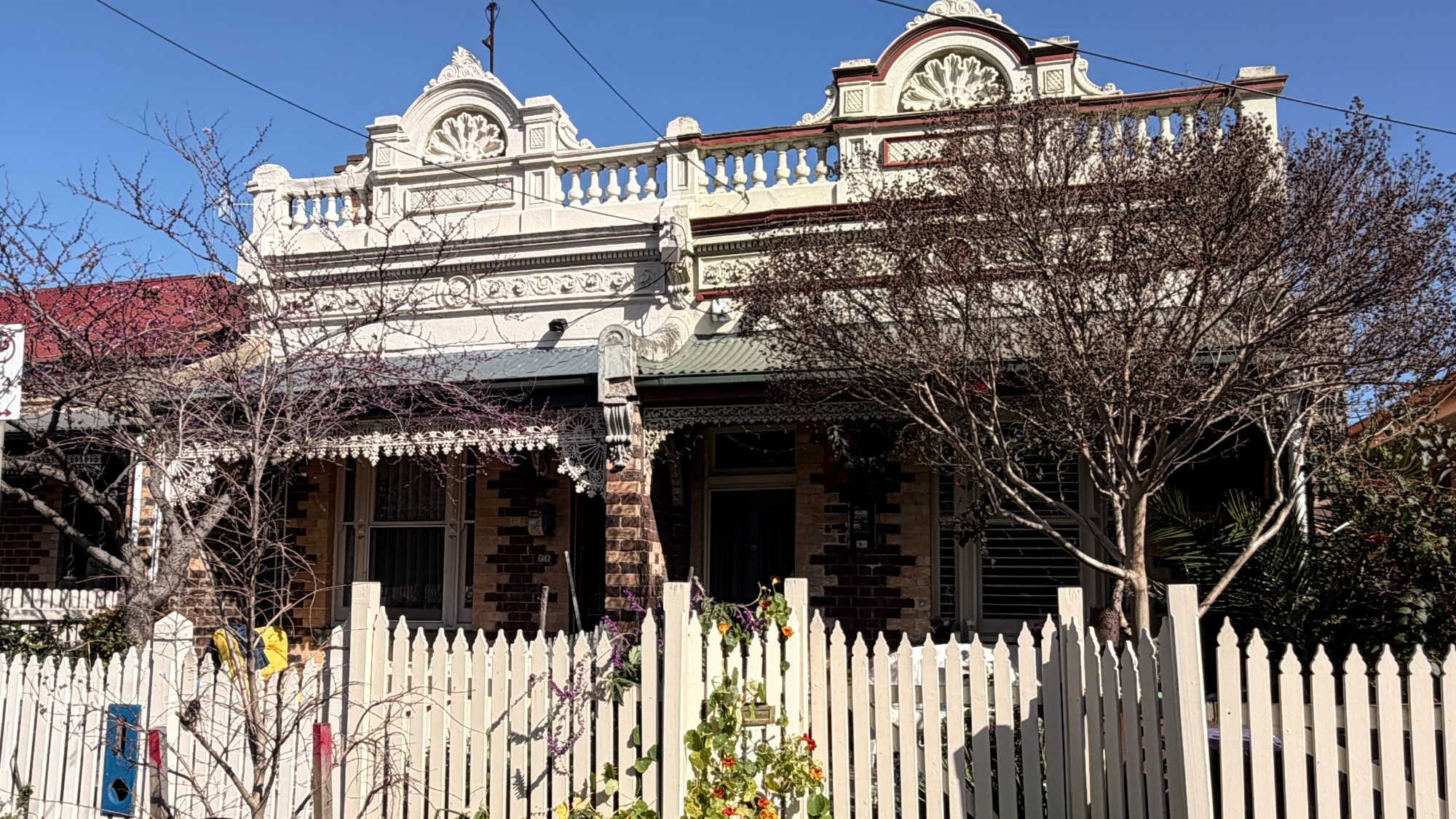 Single-storey Victorian home in Abbotsford with an ornate rendered parapet, cast-iron lacework and a white picket fence