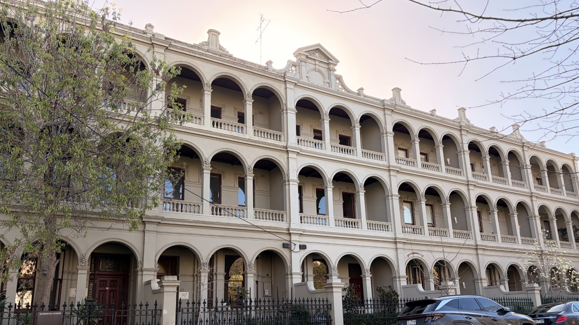 Three-storey rendered terrace row in Carlton with arched colonnades and balustraded verandahs