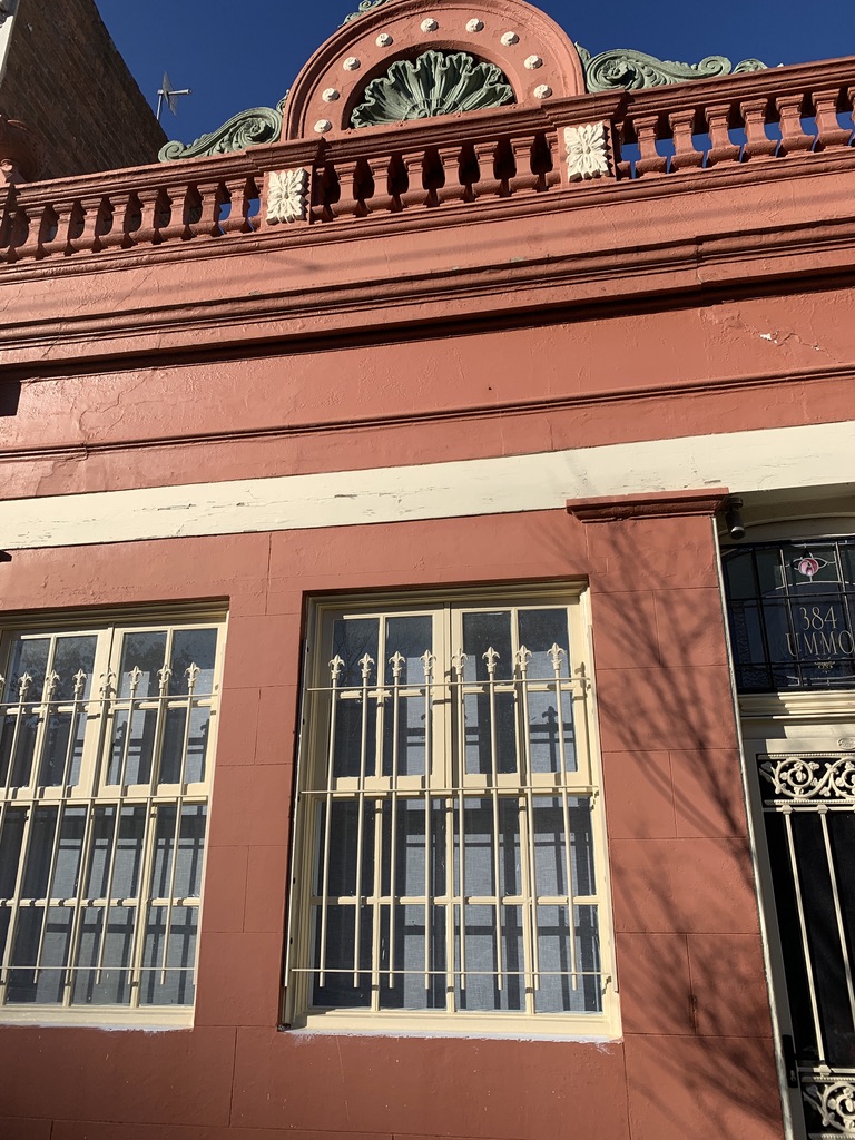 Close-up of the ornate Victorian parapet and window ironwork at 384 Drummond Street Carlton, showing the decorative render and heritage detail after repainting by Melbourne City Maintenance