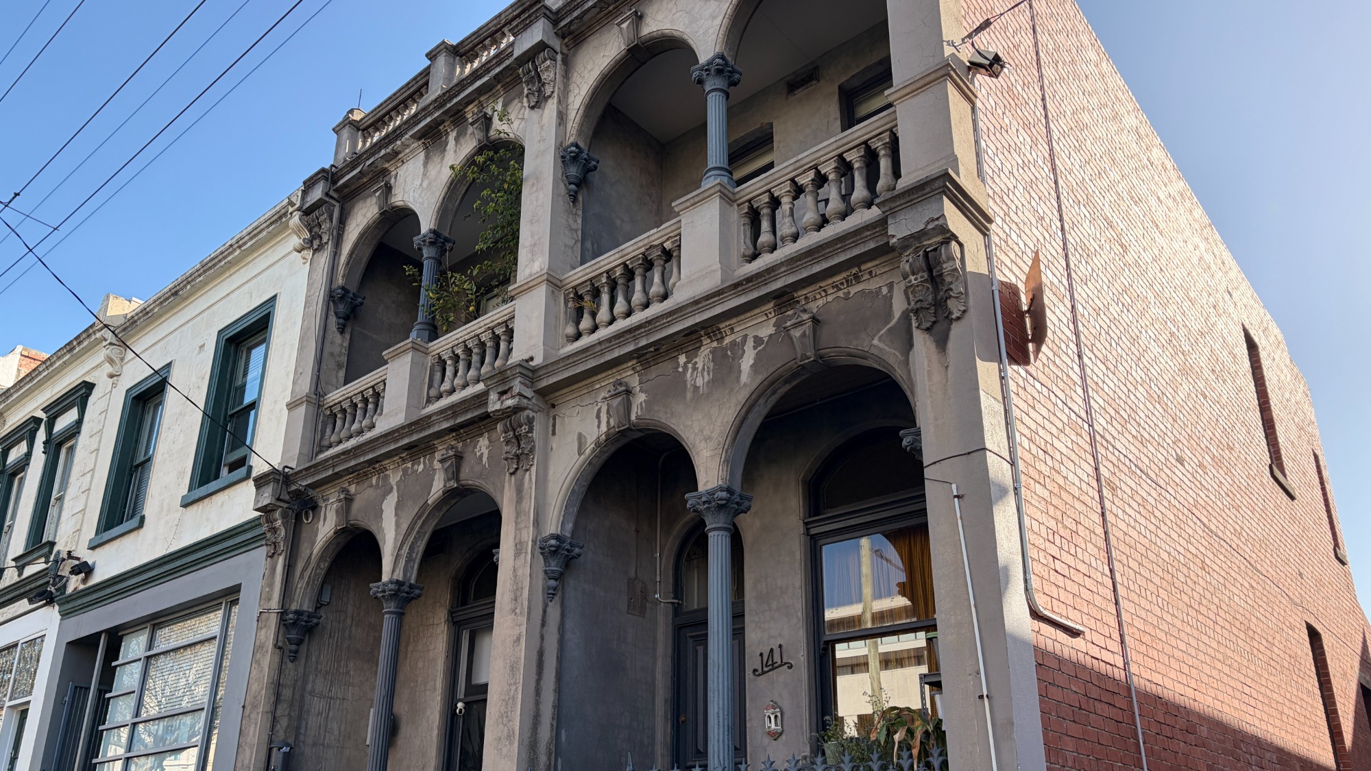 Two-storey Victorian terrace in North Melbourne with weathered render, decorative cement columns and a balustraded balcony showing surface decay