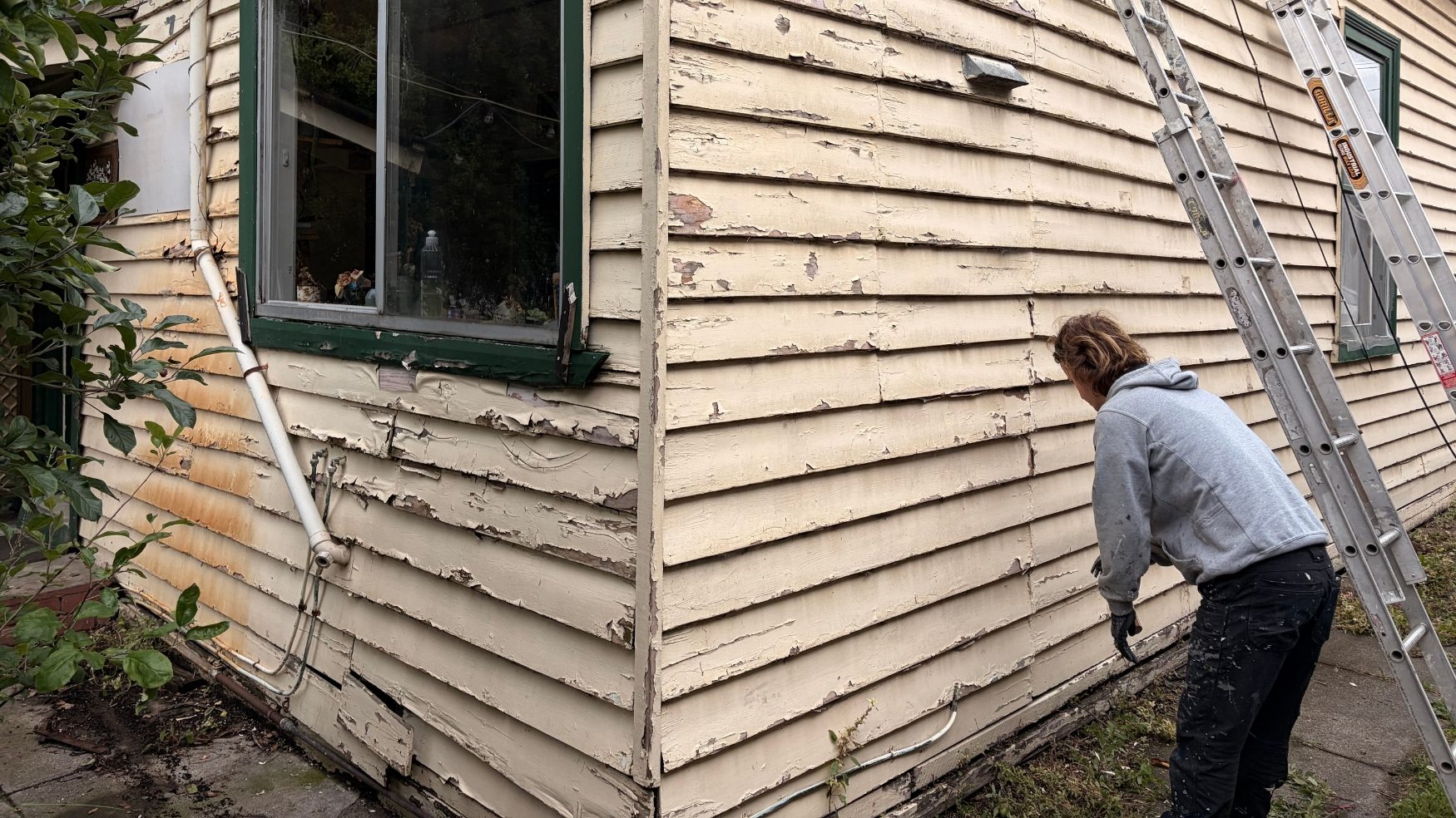 Melbourne City Maintenance tradesperson scraping failed paint from a Northcote weatherboard wall